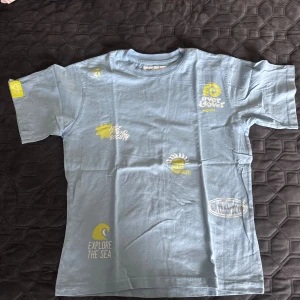 Ljusblå t-shirt med tryck från Zara - Ljusblå t-shirt från Zara med coola tryck i gult och vitt, bland annat 'Explore the Sea' och 'Over & Over Again'. Klassisk rund hals och korta ärmar. Perfekt för dig som gillar en avslappnad och trendig stil.