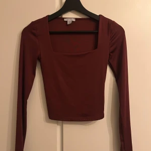 Vinröd långärmad topp  - Säljer en vinröd långärmad topp med fyrkantig urringning och croppad passform. Tunn och mjuk polyester som sitter snyggt på kroppen. Perfekt för dig som gillar stilrena och enkla plagg med modern touch.