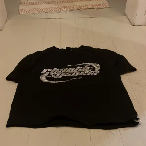 Svart t-shirt FSBN med strassprint - Svart t-shirt från FSBN i relaxed fit, storlek XS. Framsidan har ett stort, glittrigt strassmotiv med texten 'chaotic system' i silver. Klassisk rund hals och korta ärmar. Perfekt för dig som gillar statement-plagg med lite edge.