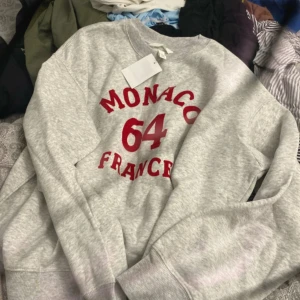Grå sweatshirt Monaco 64 S - Grå sweatshirt från H&M med röd text 'Monaco 64 France' på bröstet. Tröjan har rund hals, ribbade muddar och är långärmad. Perfekt för dig som gillar sportig och avslappnad stil. Materialet är mjuk bomullsmix. TVÅ FÖR 200kr En för 100kr