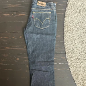 Levi's 572 Bootcut jeans mörkblå 28/32 - Mörkblå Levi's 572 Bootcut jeans med klassiska kontrastsömmar och femficksdesign. Snygg bootcut-modell som ger en schysst siluett och passar perfekt till sneakers eller boots. Tillverkade i slitstarkt denim med dragkedja och knapp framtill.