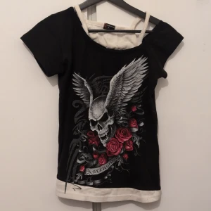 Dödskalle med vingar - Tröja med tryck. Ena ärmen är tänkt att ha längre ned, det är därför de är olika långa ärmar. Illusion av ett linne under men det vita tyget är samma tröja men man kan klippa av det om man vill. Det vita är avklippt som syns på sista bilden.