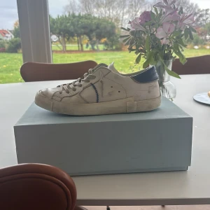 Philippe Model vita sneakers strl 40 - Säljer ett par Philippe Model PRSX Low Man sneakers i vitt skinn med blå detaljer på häl och sidor. Klassisk låg modell med snörning och platt sula. Snygg broderad detalj på sidan och mörkblå yttersula. Perfekta för en clean och stilren look. Köpta nya för 3800kr prisklass kan såklart diskuteras!