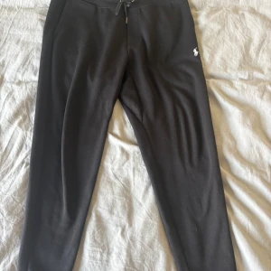 Svarta mjukisbyxor Polo Ralph Lauren XL - Svarta mjukisbyxor från Polo Ralph Lauren i storlek XL. Byxorna har dragsko i midjan, ribbade muddar vid bensluten och en broderad vit logga på låret. Sköna och stilrena, perfekta för chill eller träning.