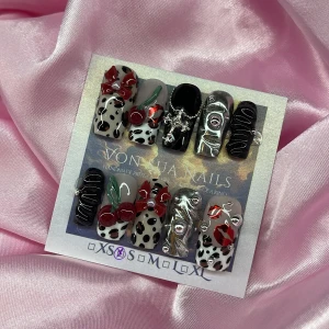 CherryKiss (S);Medium Square;Curved - Unika handgjorda press-on naglar med cool 3D-design i svart, silver och nude. Dekorerade med röda rosetter, körsbär, pärlor, kors och läppar. Mix av handmålade leopardmöbster, metallic och glansiga detaljer. Passar dig som vill sticka ut med kreativa och edgy naglar. S: 15 mm, 11,5 mm, 12 mm, 11 mm, 9 mm 