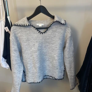 Grå stickad tröja med krage & svarta detaljer - Superfin grå stickad tröja från Gina Tricot med bred krage och v-ringning. Svarta virkade detaljer längs krage, ärmslut och nederkant ger en unik touch. Långärmad och perfekt för lager-på-lager under höst och vinter.