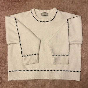 Vit stickad tröja från Neo Noir - Säljer en vit stickad tröja från Neo Noir med svarta dekorativa sömmar längs halsringning, ärmar och nederkant. Tröjan har rund hals och långa ärmar med ribbade muddar.  Använd 1 gång! Nypris ca 600