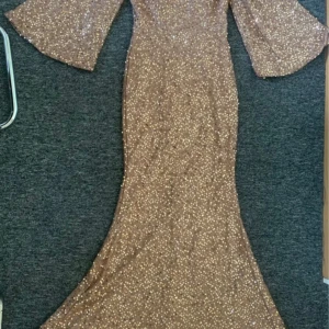 Glittrig paljett långklänning - Supersnygg långklänning i champagnefärg, täckt av glittrande paljetter. Klänningen har v-ringning, vida ärmar och figurnära passform som ger en elegant siluett. Perfekt för bal eller festliga tillfällen när du vill sticka ut. Använd en gång!