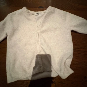 kofta  - Mysig ljusbeige kofta från Kappahl med rund hals och ribbade muddar. Koftan har knappar framtill och är långärmad, perfekt för lager-på-lager under kyliga dagar. Enkel och stilren design som passar till det mesta.