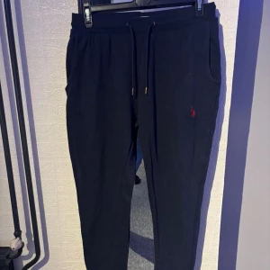 ralph lauren byxor  - Mörkblå mjukisbyxor från U.S. Polo Assn. med dragsko i midjan och sidofickor. Byxorna har en liten röd logga broderad på ena benet och är tillverkade i mjukt bomullsmaterial. Perfekta för en chill och avslappnad stil. Knappt använda!