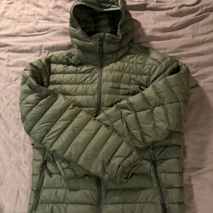 Grön dunjacka Peak Performance L - Säljer en grön down liner dunjacka från Peak Performance i storlek L. Jackan har huva, dragkedja framtill och två sidofickor med dragkedja. Lätt och smidig modell som är perfekt för kyliga dagar. Klassisk quiltad design och stilren look. Jackan är använd några få gånger och är i mycket fint skick. Ny pris är 3000kr