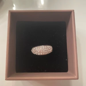 Glittrig silverring med stenar - Säljer en snygg silverfärgad ring med massor av glittrande stenar som täcker hela ovansidan. Ringen har en rundad form och är perfekt för dig som gillar att sticka ut med dina accessoarer. 