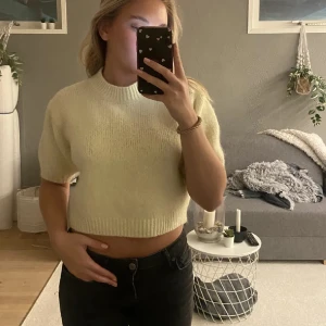 Ljusgul croppad stickad topp - Superfin ljusgul croppad stickad topp med korta ärmar och ribbad kant vid hals och nederdel. Mjuk och fluffig känsla, perfekt att styla med höga jeans eller kjol. Enkel design som ändå känns trendig och fräsch.