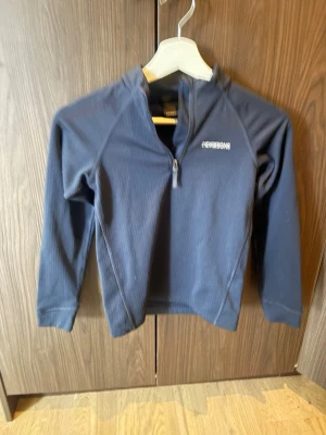 Marinblå långärmad topp från didrikson - Säljer en marinblå långärmad topp från didrikson med diskret ribbad struktur och halv dragkedja framtill. Perfekt för lager-på-lager och outdoor-aktiviteter. Everest-logga på bröstet och mjukt, stretchigt material.