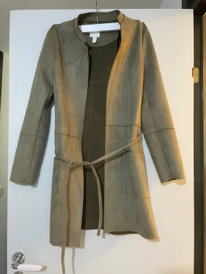 Beige mocka kappa med bälte - Snygg beige kappa i mjuk mockaimitation från H&M.  långa ärmar och knytskärp i midjan för en clean look. Perfekt för dig som gillar stilrena plagg med enkel design.