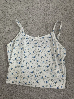 vit blommig topp - en vit blommig liten topp med små blå blommor på sig. den har en liten rosett. 