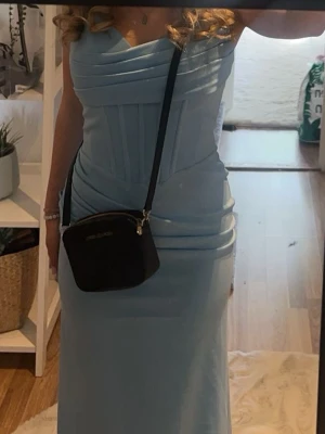 Ljusblå långklänning med snörning - Supersnygg ljusblå långklänning med figurnära passform och slits på sidan. Klänningen har omlott-detaljer upptill, snörning i ryggen och är axelbandslös. Perfekt för bal eller festliga tillfällen. Materialet känns mjukt och följsamt.