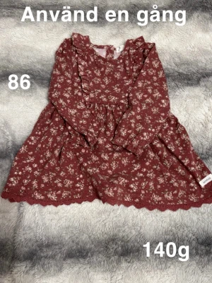 Blommig vinröd klänning från Newbie  - Supersöt vinröd klänning från Newbie med små blommor. Klänningen har volangdetaljer vid axlarna, lång ärm och spetskant nertill. Perfekt för dig som gillar romantisk stil och fina detaljer.🌸 Använd en gång. Storlek 86