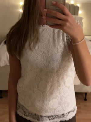 Vit spetsblus med kort ärm - Säljer en superfin vit blus i spets med korta ärmar och rund hals. Blusen har ett detaljerat spetsmönster och vågig kant längst ner. Perfekt att styla med jeans eller kjol för en fräsch look.