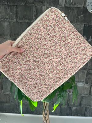 Blommig quiltad datorväska - Supersöt quiltad datorväska med småblommigt mönster i rosa, grönt och beige. Den har ett fack med dragkedja innuti. Den är sparsamt använd. Säljer pga att den inte kommer till användning. Priset kan diskuteras. 