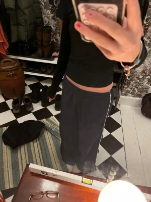 Mörkblå mjukisbyxor med vita ränder - Säljer ett par mörkblå mjukisbyxor med vita ränder längs sidorna. Byxorna har resårmidja med snörning och är tillverkade i mjukt bomullsmaterial. Passformen är loose och benen är raka för en chill vibe.