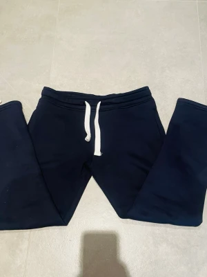 Russemerch byxor - Mörkblå mjukisbyxor från Russedress i storlek S. Byxorna har vita snören i midjan och är gjorda i mjukt bomullsmaterial. Perfekta för chill dagar eller när du vill vara extra bekväm. Klassisk passform och enkel design.