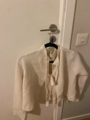 Vit ribbad kofta med knytband - Säljer en superfin vit ribbad kofta med långa ärmar och knytband framtill. Koftan är stickad och har en croppad passform som ger en trendig look. Perfekt att slänga över en topp för extra stilpoäng.