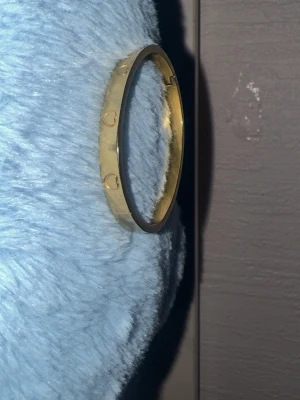 Guldväst med hjärtdetaljer från DARK - Säljer en snygg guldväst från DARK med ingraverade hjärtan runt om. Västen har en klassisk, rak form och är tillverkad i ett syntetmaterial med metallisk finish. Perfekt för dig som vill sticka ut med en unik detalj i din outfit. DEN ÄR ÄNTA 