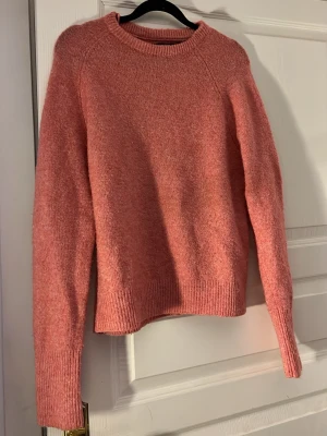 Rosa stickad tröja med lång ärm - Mysig rosa stickad tröja med rund hals och långa ärmar. Tröjan har en enkel design utan mönster eller detaljer, perfekt att matcha med jeans eller kjol. Materialet känns mjukt och skönt mot huden och färgen är varm och fräsch.