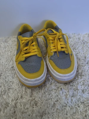 Nike Air Force 1 gul och grå - Nike Air Force 1 sneakers i en riktigt snygg färgkombo av gult och grått. Skorna har klassisk låg siluett, vit sula och gula snören. Tillverkade i skinn med perforerad tå och ikonisk swoosh på sidan. Perfekta för dig som vill sticka ut med färg!