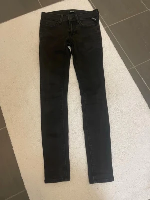 Svarta skinny jeans från Replay - Säljer ett par svarta skinny jeans från Replay med klassisk femficksdesign och snygga detaljer på bakfickorna. Jeansen har normal midja och är tillverkade i stretchigt jeansmaterial för en tight passform. Perfekta till sneakers eller boots.