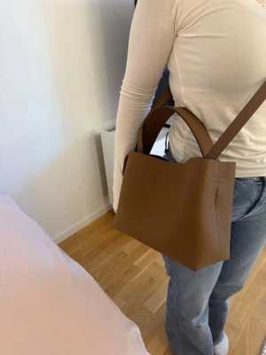 Arket läderväska  - Säljer denna fina läderväska från Arket. Man kan bära den som en handväska eller axelremsväska då man kan ta av bandet. Väskan har ett fack inuti som är perfekt till nycklar, plånbok eller liknande. Den har magnetlås och guldiga detaljer. Perfekt väska att tex ha på jobb som får plats med mycket. Nypris ca 2000 kr, endast använd vid fåtal tillfällen. Tar bud och kan gå ner i pris vid snabb affär.