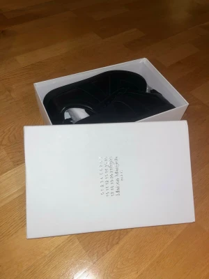 Maison Margiela svarta sneakers - Maison Margiela sneakers i helsvart med klassisk låg siluett. Skorna har ovandel i skinn och mocka, med matchande svarta snören och platt sula. Snygg minimalistisk design och diskreta detaljer som gör dem riktigt stilrena.