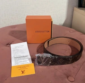 Louis Vuitton monogram bälte brun - Säljer ett Louis Vuitton bälte i klassiskt monogrammönster med stor LV-logga på metallspännet. Bältet är brunt med beige insida och har exklusiv känsla. Kommer med originalbox och certifikat. Perfekt accessoar för att lyfta din outfit.