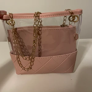 Rosa axelväska - Snygg rosa axelväska med snygga detaljer på utsidan. Guldfärgad kedja. Har en mindre plånbok inuti som man kan lägga mindre saker i!