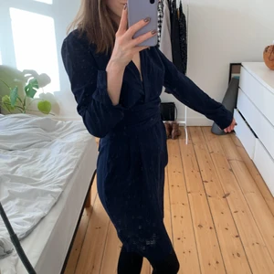 Tætsiddende kjole med V-udskæring - Kjolen lynes i siden og har bindebånd i taljen. Den sidder stramt om kroppen hele vejen ned og har en dyb V-udskæring.