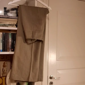 Kostymbyxor  - Brun/beiga kostymbyxor från hm, Jättefint skick! Högmidjade och långa, vida byxben. Midjemått ca 71 cm & innerbensmått 78 cm. Köparen står för frakten. Bara å skriva för fler bilder/info! 🧡
