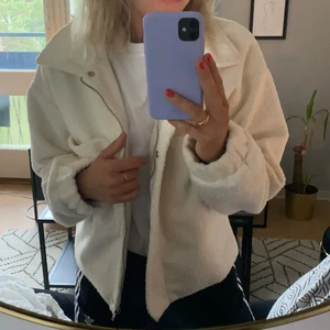 Vit teddyjacka - Vit/benvit teddyjacka från Nelly. Jackan har två stora fickor samt dragkedja och knappar. Storlek 42. Använd ett fåtal gånger så jackan är i gott skick!