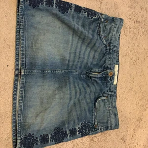 Jeans kjol  - En jeans kjol med blommor på sidorna. 