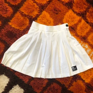 Tenniskjol - Säljer denna jättefina tenniskjol som är väldigt inne just nu! Den har dold dragkedja och en fin liten knapp på sidan. Från Bershka, storlek XS. Den är aldrig använd då den tyvärr var lite för liten för mig och jag glömde returnera, så den är i nyskick! Går att mötas upp i Hagfors eller så skickas den med posten där köparen står för frakten!