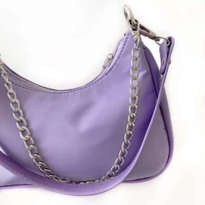 Lila väska - Lila baguette väska med silver detaljer och avtagningsbara band. Väskan är i polyester material. Väska med originalband 250kr Väska med både originalband & kedjeband 300kr