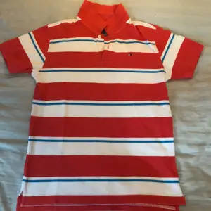 Randig polo tröja i färgerna, ljusblå, vit och röd/orange. Tröjan är i mycket fint skick. Den passar 16-18 år (L).