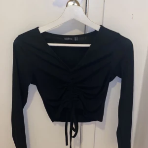 Svart tröja ifrån Boohoo - Svart tröja med snören i mitten som man drar åt beroende hur ihopslagen man vill ha den, använd fåtal gånger som ny.
