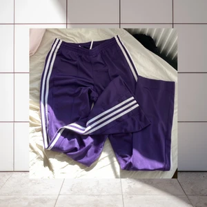 Lila Adidas trackpants 😻 - Sååå fina, mörklila Adidasbyxor med vita ränder. Märket sitter på höger baksida, längst upp vid midjan. Resår med snören som kan knytas. Vida ben. Storleken är svår att utse efter lappen, men jag tror det är strl 164? Passar nog en XS. Jag ansvarar inte för postens slarv!