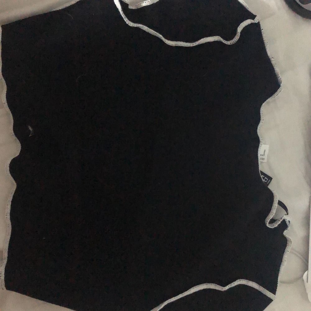 En svart tröja med vita sömmar som är öppen till bröstkorgen. den sitter bra och man kan snöra tröjan hur man vill. Ganska kort. . Toppar.
