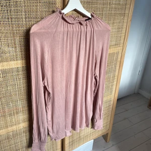 Blus med volangdetaljer - Luftig och mjuk blus från Lager 157 i storlek S. Fin gammelrosa färg och volangdetaljer runt kragen och fina muddar vid ärmslut. Knappt använd så väldigt bra skick.