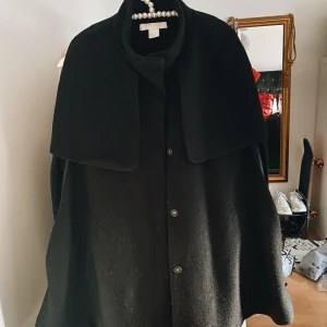 Cape från H&M - Svart cape från H&m i 80% polyester & 20% ull. Den är ganska varm och i lite tjockare material. Lite nopprig i fram, därav priset.