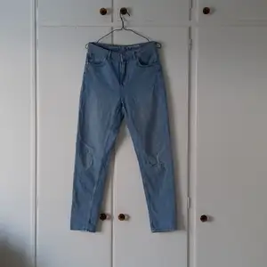 Ett par blå jeans, Never Denim, i storlek M. Det är en design med hål på vänster knä. Byxan smalnar av vid ankeln. Använda men i fint skicka, fick dem men aldrig själv använt dem så säljer. Pris: 80 + frakt