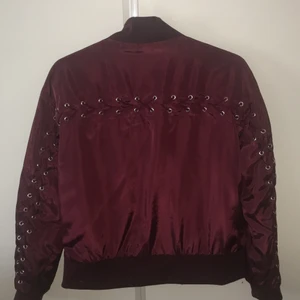 Bombarjacka  - Riktigt cool Bombarjacka från Na-kd. Snörningsdetalj på ryggen som går ut längs med armarna. I vinrött. Tunn och skön. 