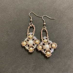 Handgjorda örhängen - Dessa örhängen har jag gjort själv.   De är gjorda med små glaspärlor.  Genomskinliga glaskristaller.  En stor vit plastpärla i mitten och vaniljfärgade plastpärlor på kanterna.  Örhänget är av metal   Själva hänget är ca 4 cm lång. 